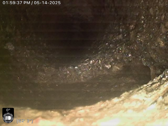 Camera view inside a pipe showing rough, dark interior surfaces with visible buildup. Timestamp reads 01:59:37 PM, 05-14-2025. Temperature and angle indicators are also present.